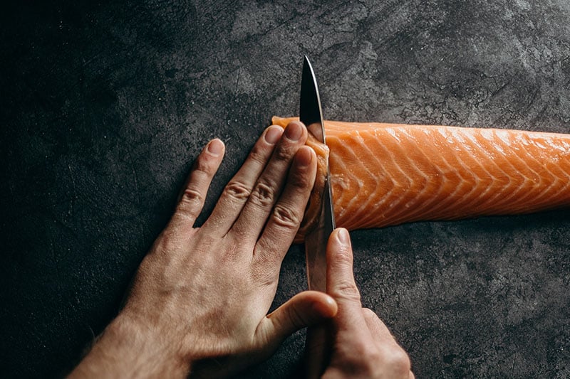 Handen met mes die zalm snijden